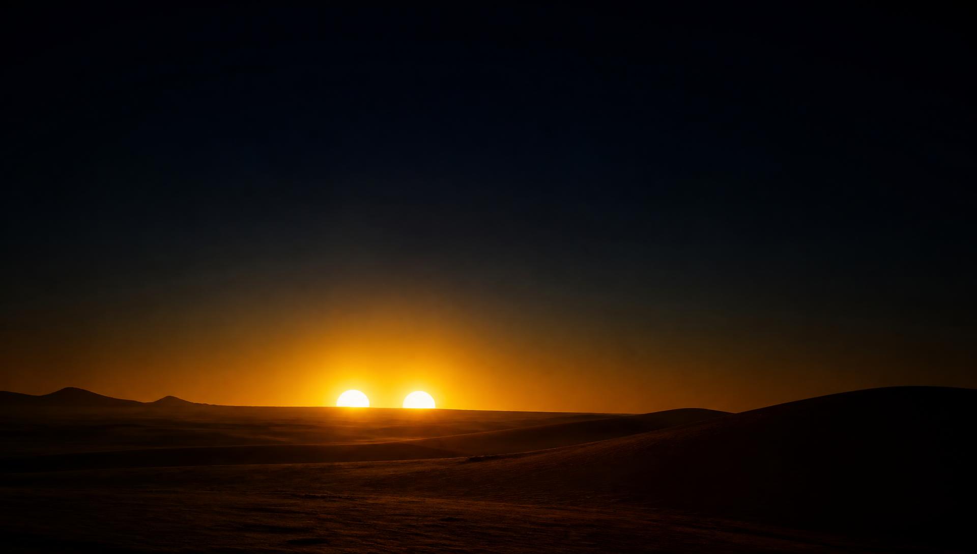 Two suns setting over a desert horizon